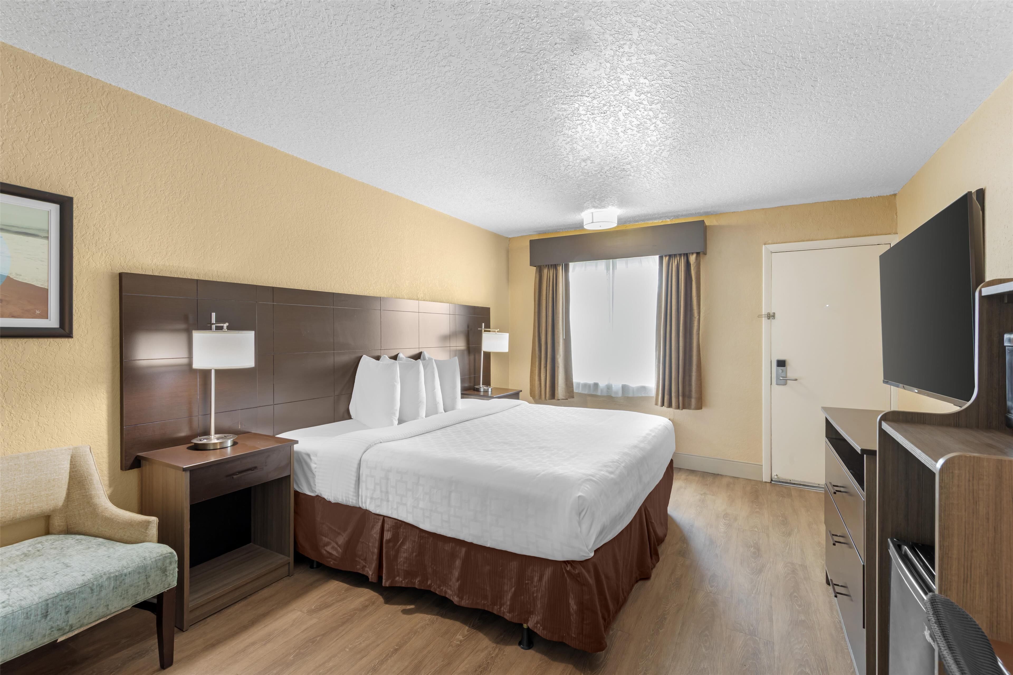 A hotel room with a large bed, a desk with a lamp, a TV, and a chair.