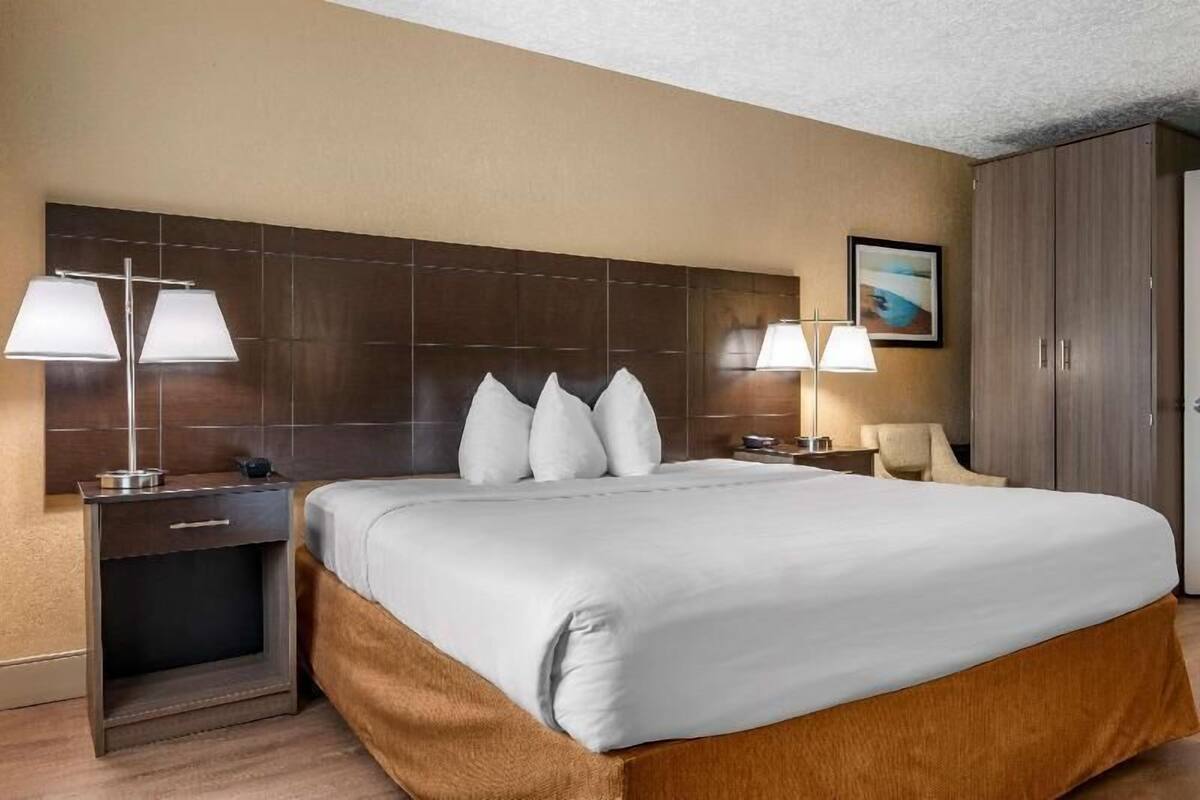 A hotel room with a large bed, two bedside lamps, a nightstand, a chair, and a wardrobe.