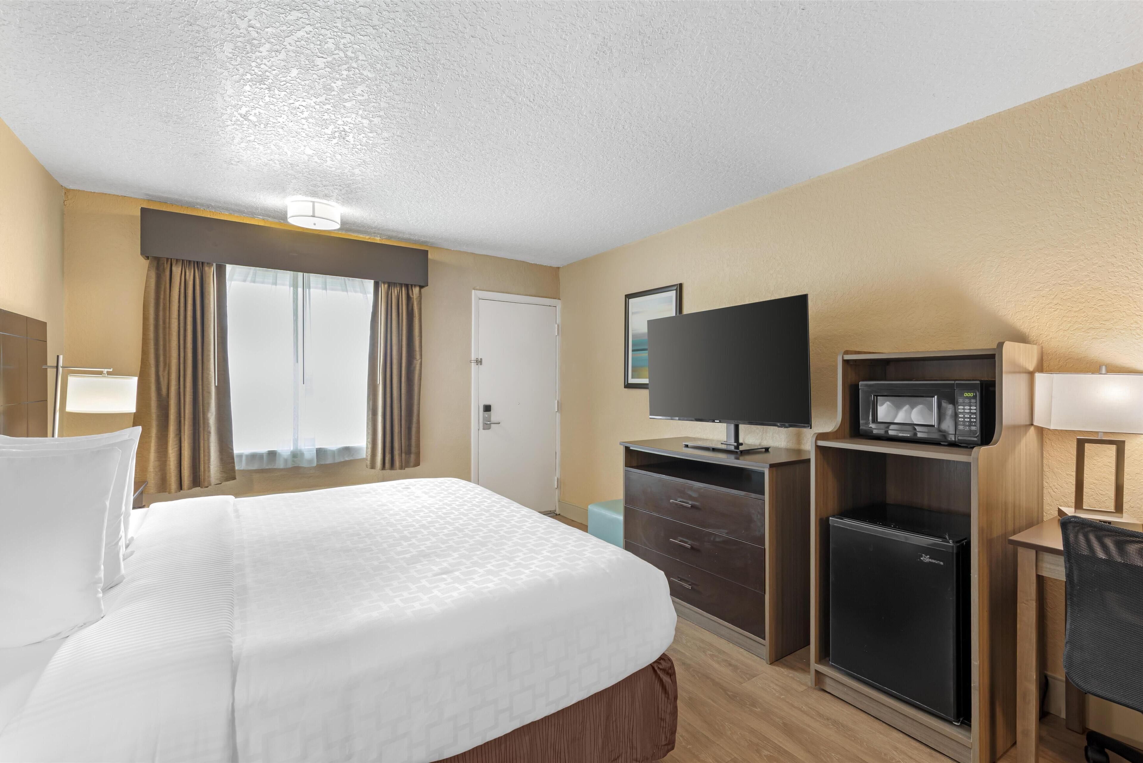 Una habitación de hotel con una cama grande, televisión, microondas y refrigerador.
