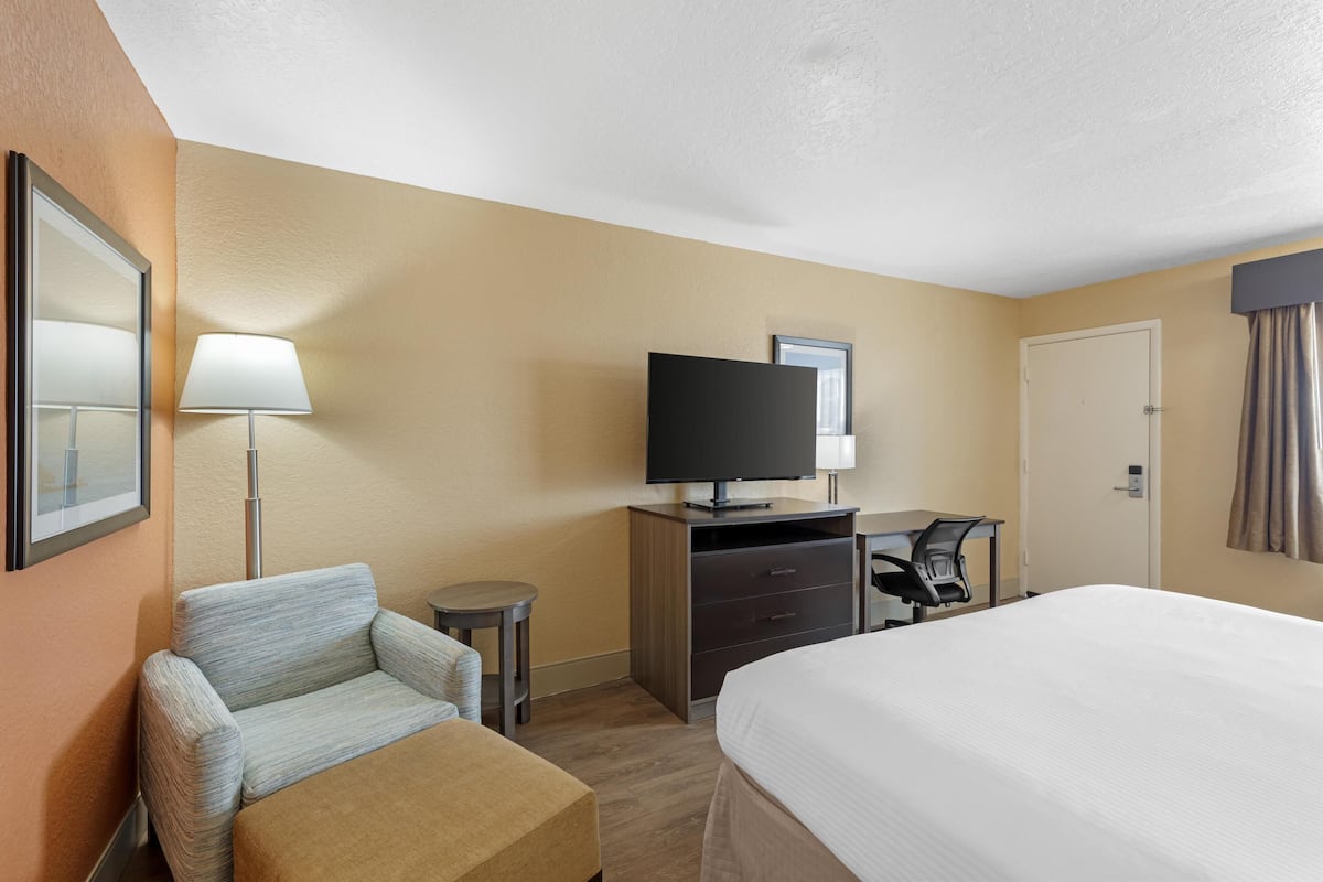 A hotel room with a bed, a sofa, a desk with a computer, a television, and a door.