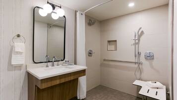 Un baño moderno con un lavamanos doble, un espejo grande con iluminación y una ducha con cabezal de ducha de mano, además de un toallero pequeño.