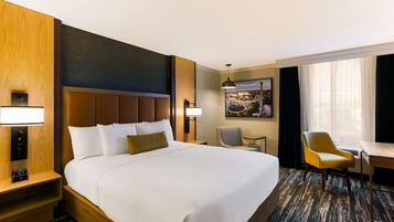A hotel room with a large bed, bedside tables with lamps, a desk, a chair, and a large window with curtains.