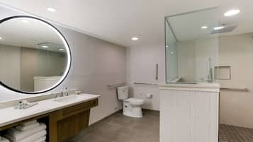 A modern bathroom with a large mirror, two sinks, a toilet, and a shower area.