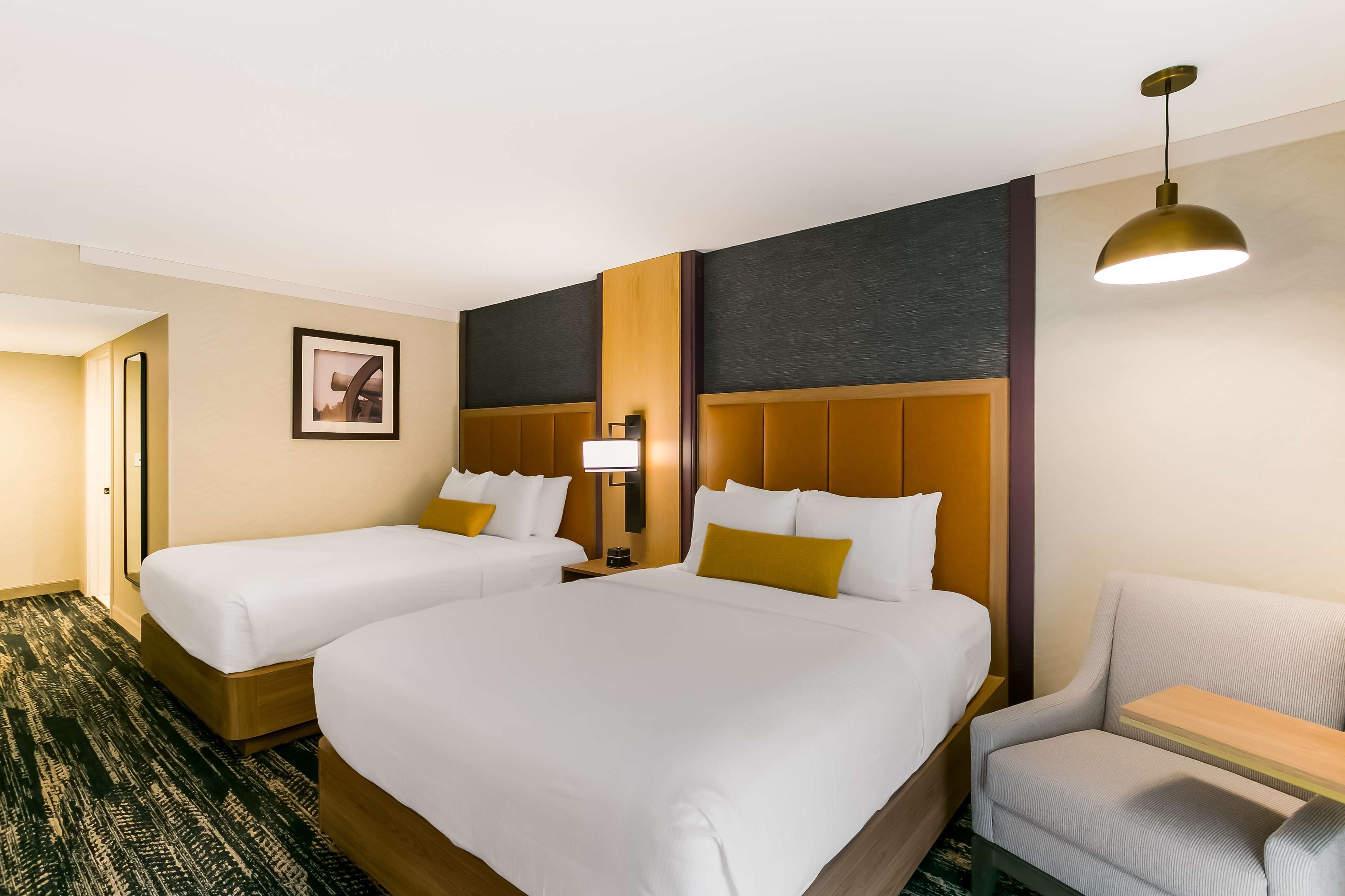 Hotellihuone, jossa on kaksi sänkyä, työpöytä, tuoli ja suuri ikkuna.