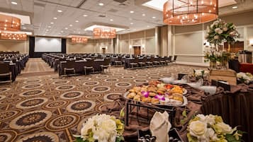 A conference room with rows of chairs, a stage, and a buffet table with food and flowers.
