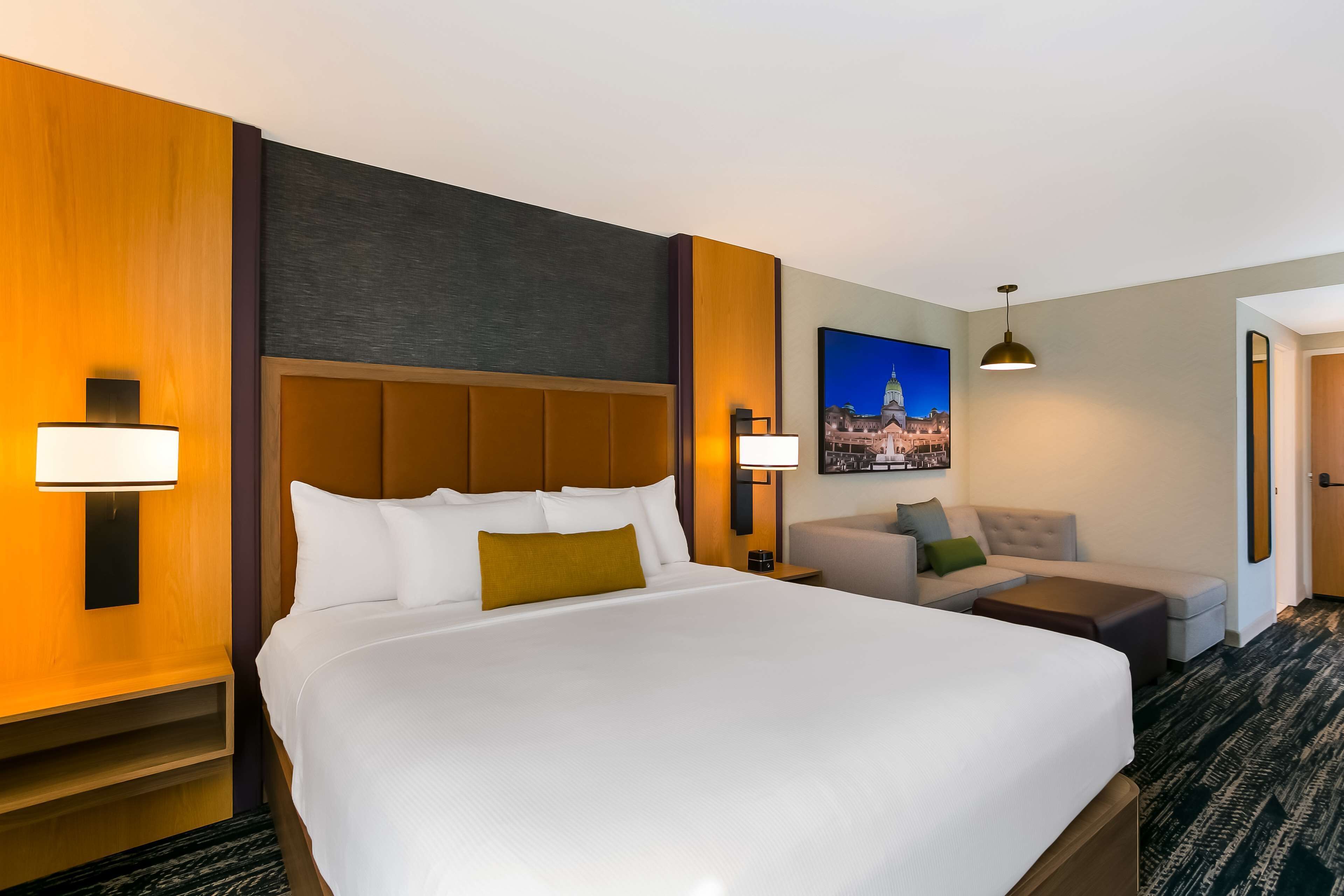 A hotel room with a large bed, a sofa, a desk, and a painting of a cityscape.
