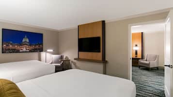 Ett hotellrum med två sängar, en platt-TV som är monterad på väggen, ett skrivbord med en lampa och en stol.