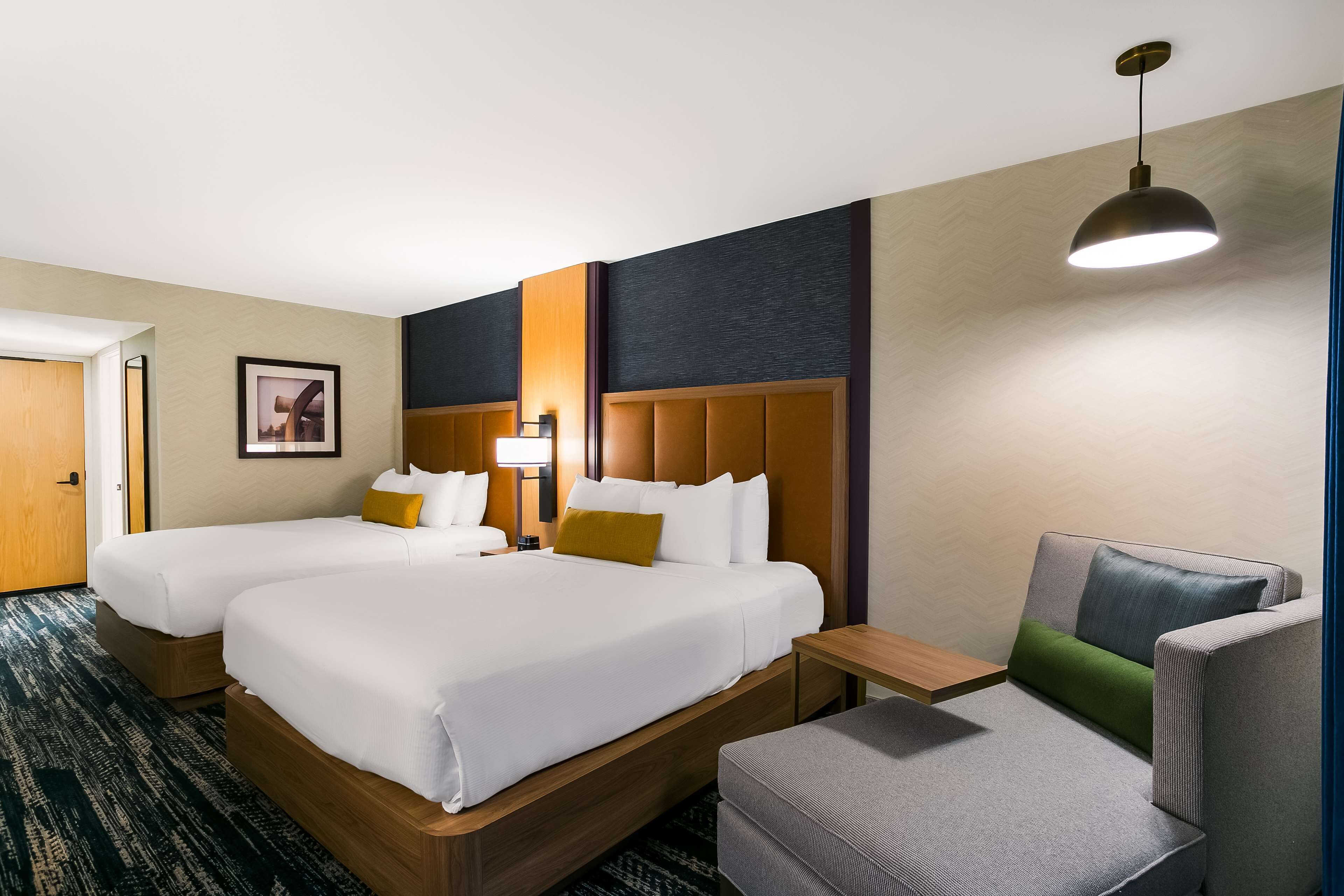 Habitación de hotel con dos camas, un sofá, una mesita y una lámpara colgante.
