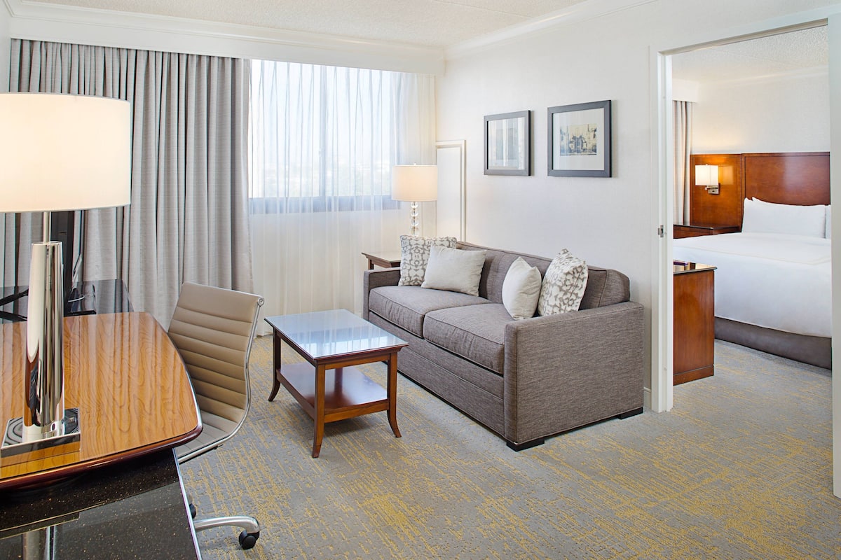 Una habitación de hotel con una cama, un sofá, una mesita, una silla y un escritorio con una lámpara.