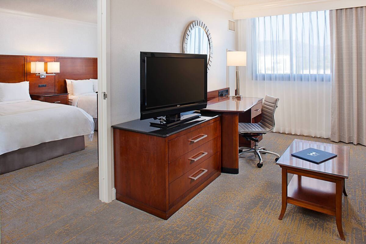 Habitación de hotel con cama, escritorio con televisor, silla y una pequeña mesa con una computadora portátil.
