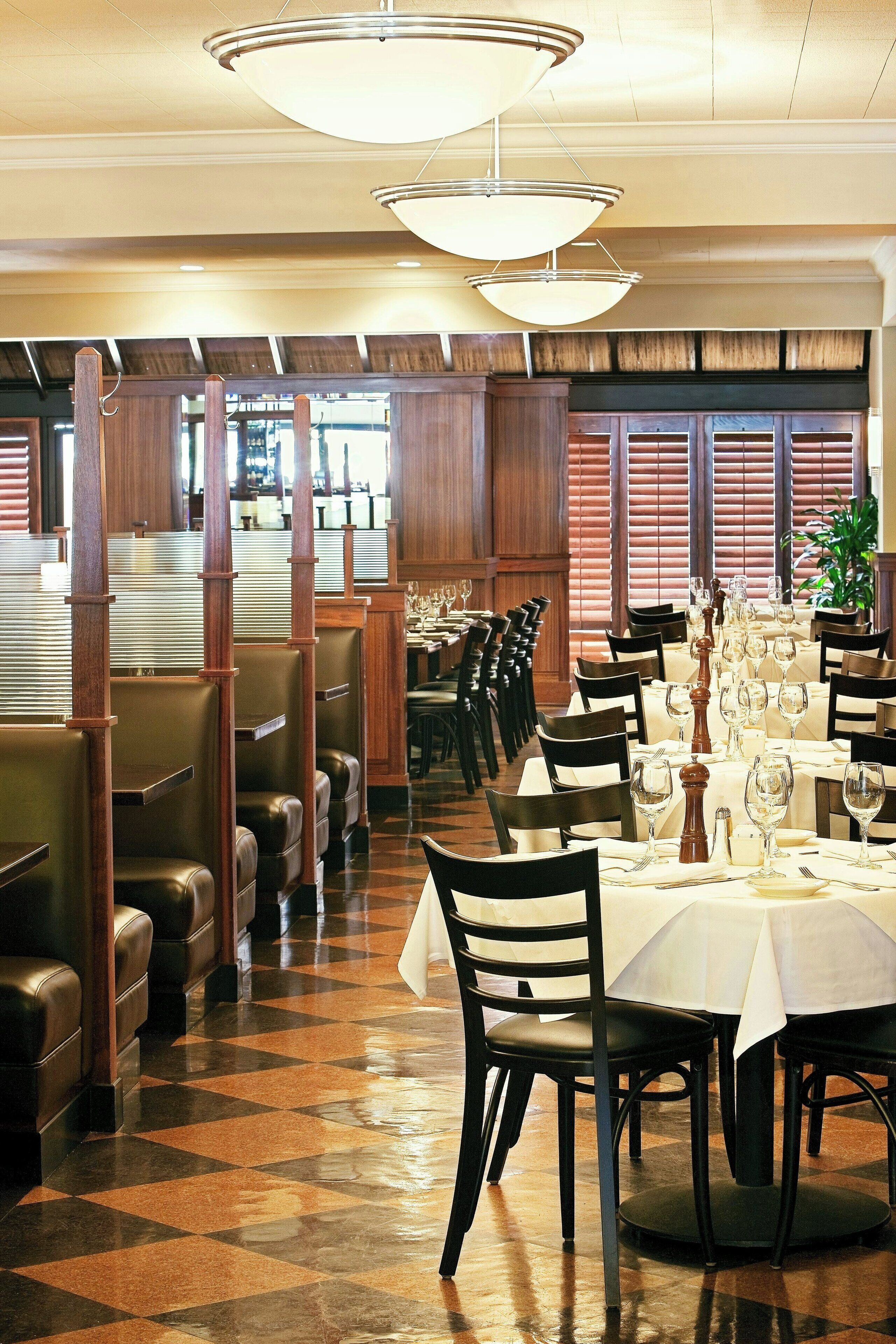 A restaurant with booth seating, round tables with white tablecloths, and a checkered floor.