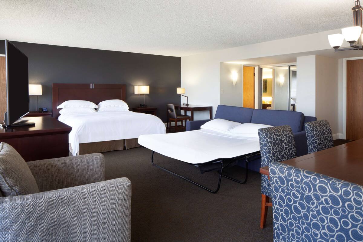 A hotel room with two beds, a desk, a chair, and a sofa.