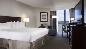 A hotel room with a large bed, a desk, a chair, a TV, and a window with a view. - Hilton Houston NASA Clear Lake (Houston)