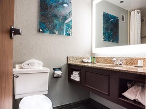 A modern bathroom with a toilet, sink, and mirror. There are towels and toiletries on the counter. - Hilton Houston NASA Clear Lake (Houston)