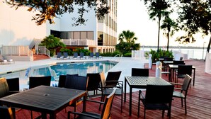 A poolside area with lounge chairs and tables, a pool, and a building with balconies. - Hilton Houston NASA Clear Lake (Houston)