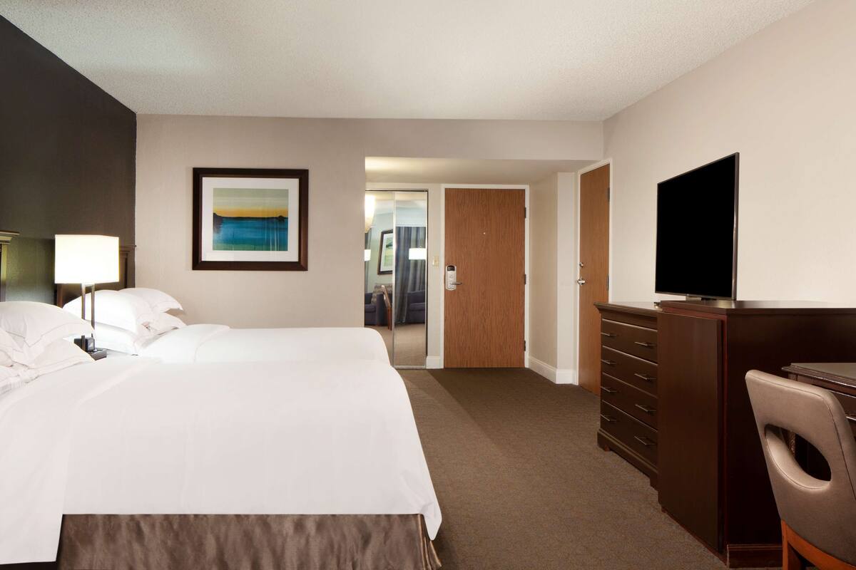 A hotel room with a large bed, a television, a dresser, and a door leading to a bathroom.