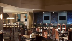 A restaurant with multiple dining tables and chairs, recessed lighting, and a patterned wall with two flat-screen TVs. - Hilton Houston NASA Clear Lake (Houston)