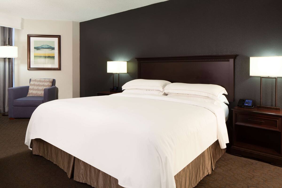 A hotel room with a large bed, two bedside tables with lamps, a chair, and a framed picture on the wall.