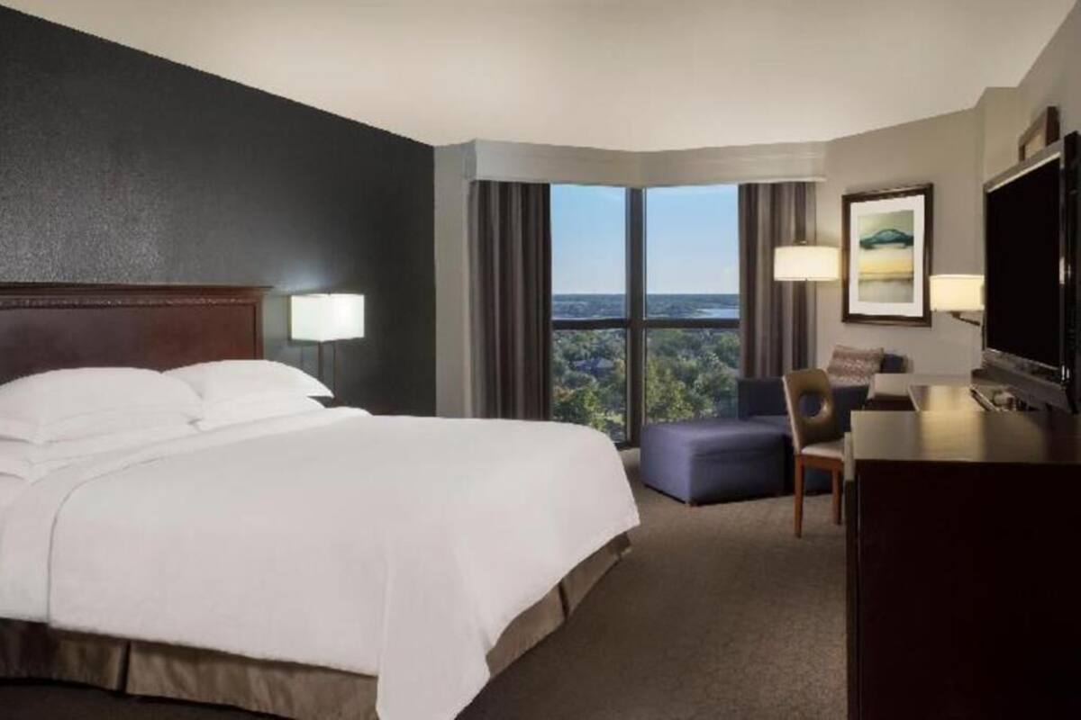 Quarto de hotel com uma cama grande, uma escrivaninha, uma cadeira, uma televisão e vista para o exterior.