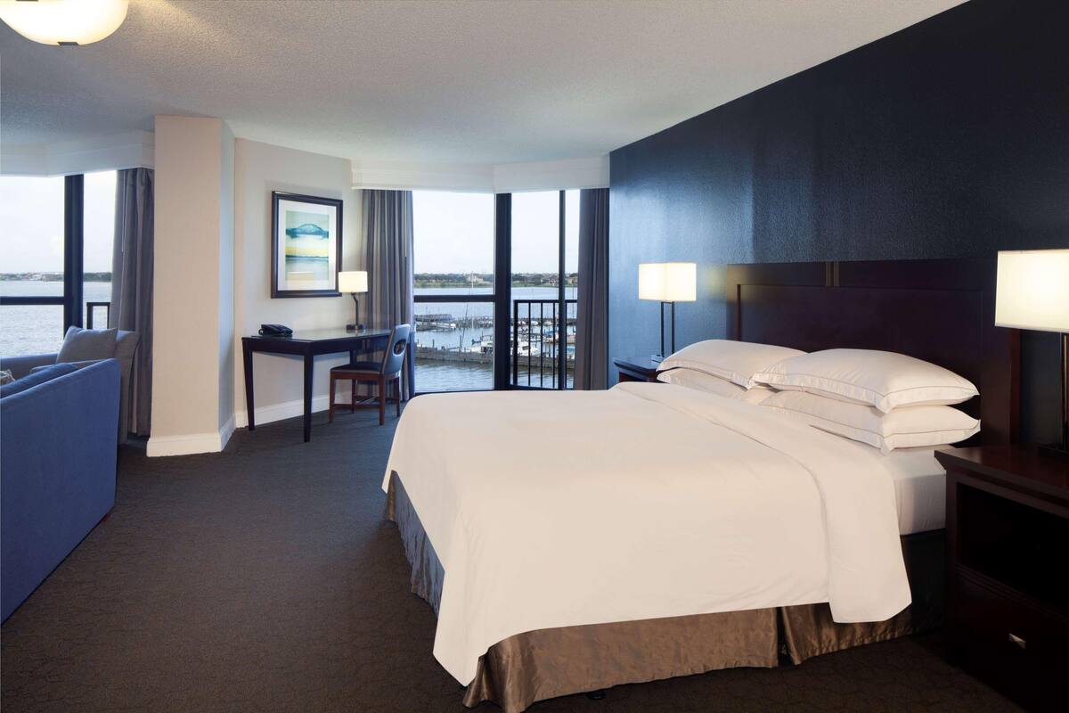 Quarto de hotel com uma cama grande, uma escrivaninha, uma cadeira e vista para a água.