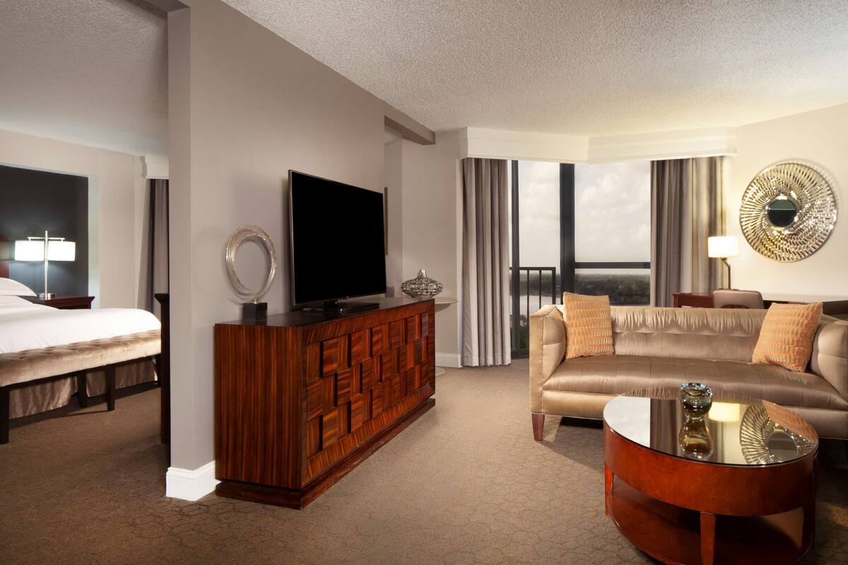 A hotel room with a bed, a TV on a wooden cabinet, a sofa, and a coffee table.