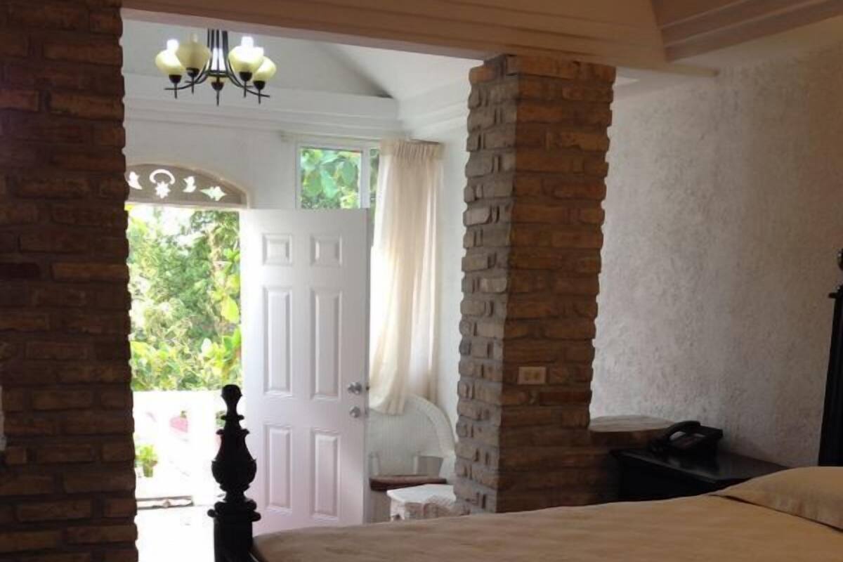 A bedroom with a large bed, a chandelier, a brick wall, and a door leading to a balcony.