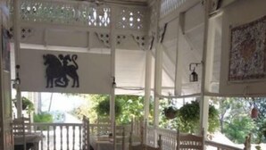 Un área de estar al aire libre techada, con sillas y mesas de madera, un techo decorativo y vistas a zonas verdes.