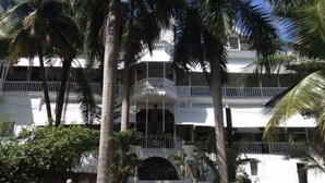 Un edificio de varios pisos con balcones, palmeras y una escalera que conduce a la entrada.