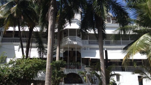 A multi-story building with balconies, palm trees, and a staircase leading to the entrance.