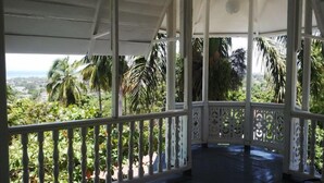 A covered outdoor area with a view of a lush landscape, including palm trees and a distant view of a town.