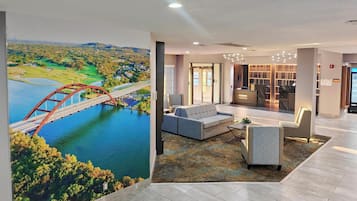 Un vestíbulo de hotel con mostrador de recepción, zona de estar y un mural de un puente sobre el agua.