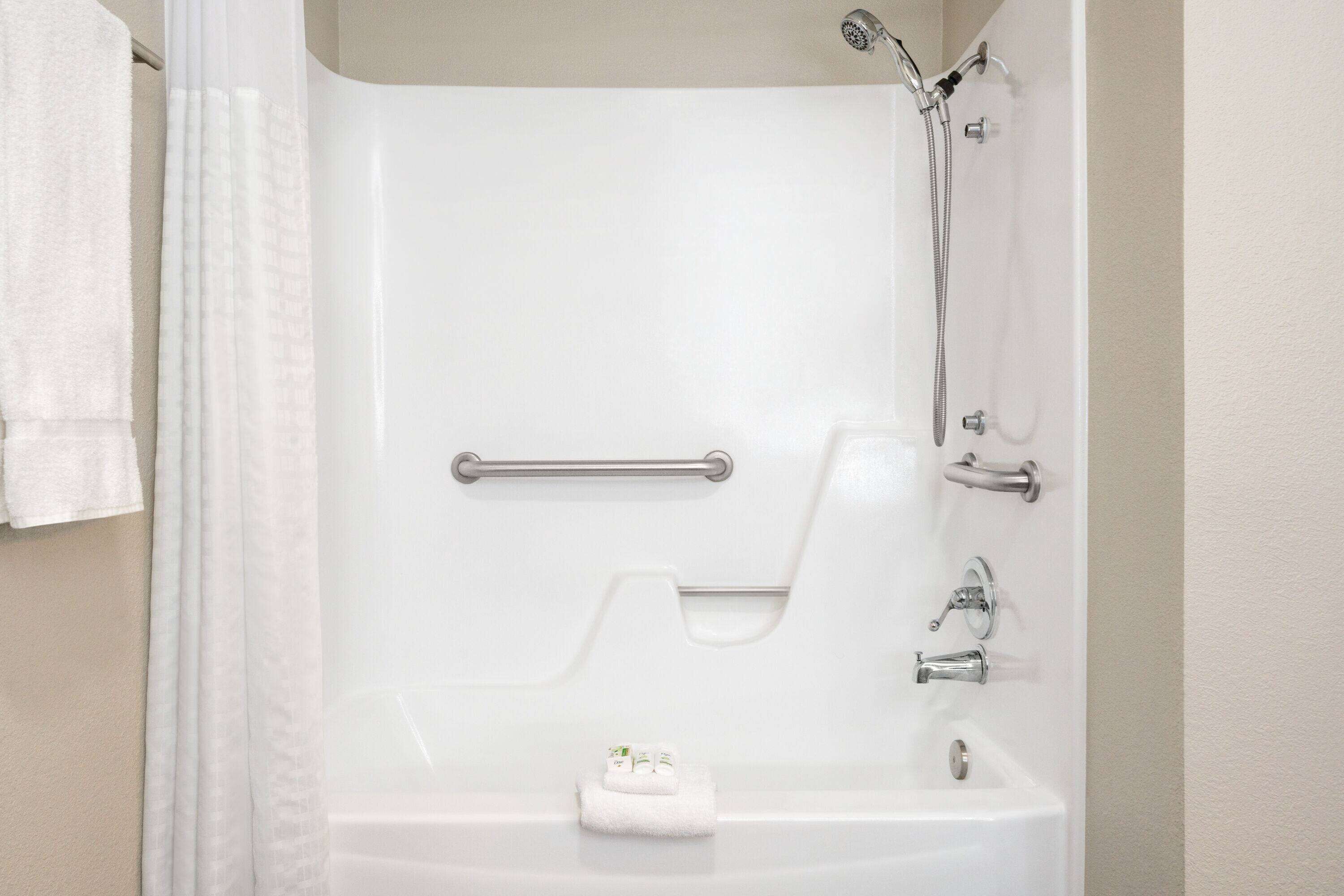 Una bañera blanca con ducha, barras de apoyo y un perchero para toallas.