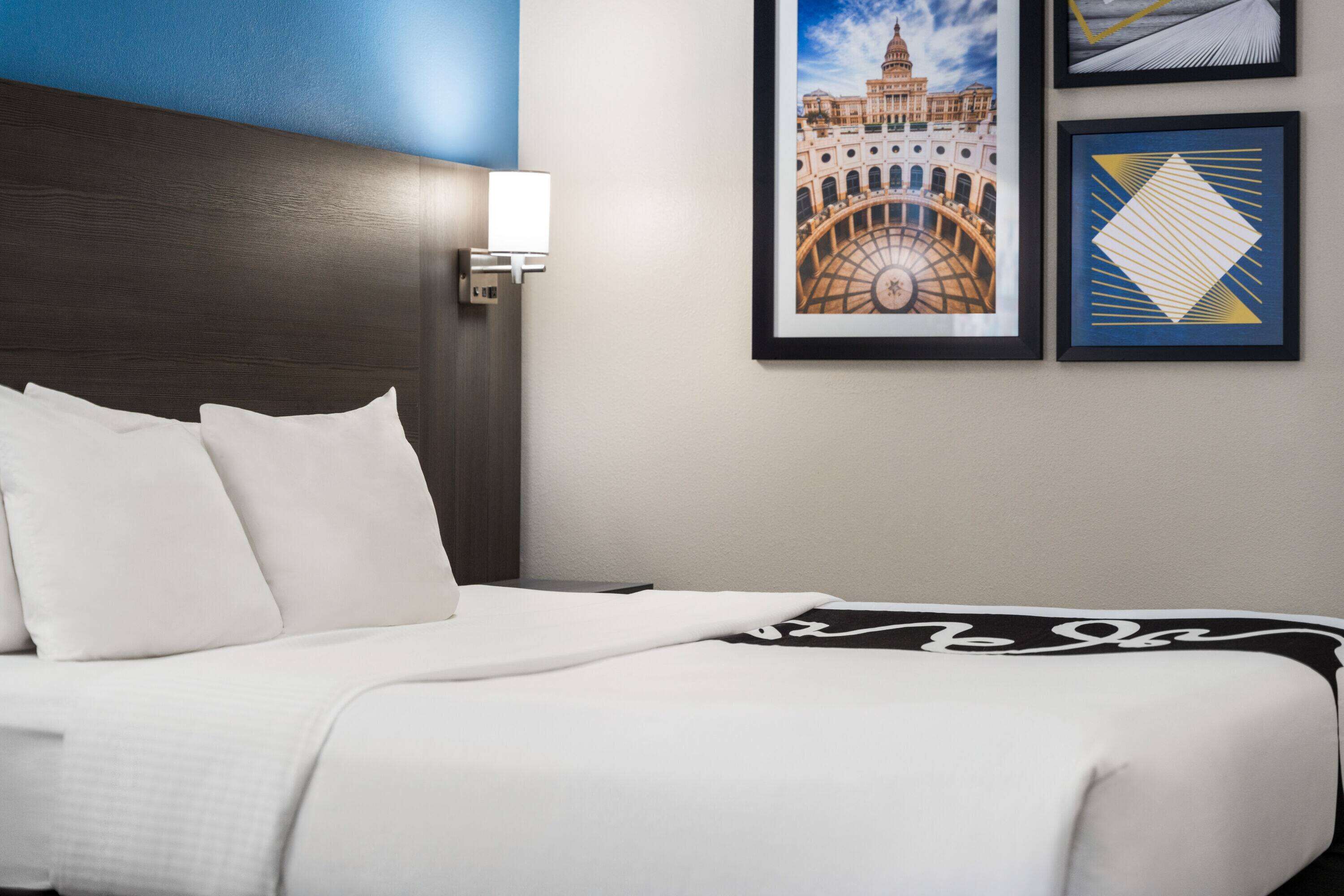 Ein Hotelzimmer mit einem ordentlich bezogenen Bett, einer Wandlampe und zwei gerahmten Bildern an der Wand.
