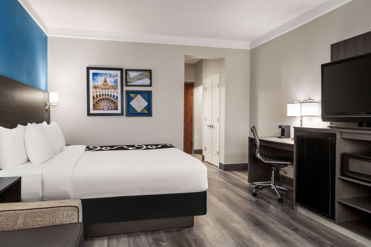 Une chambre d’hôtel avec un lit, un bureau, une chaise, une télévision et des œuvres d’art accrochées au mur.