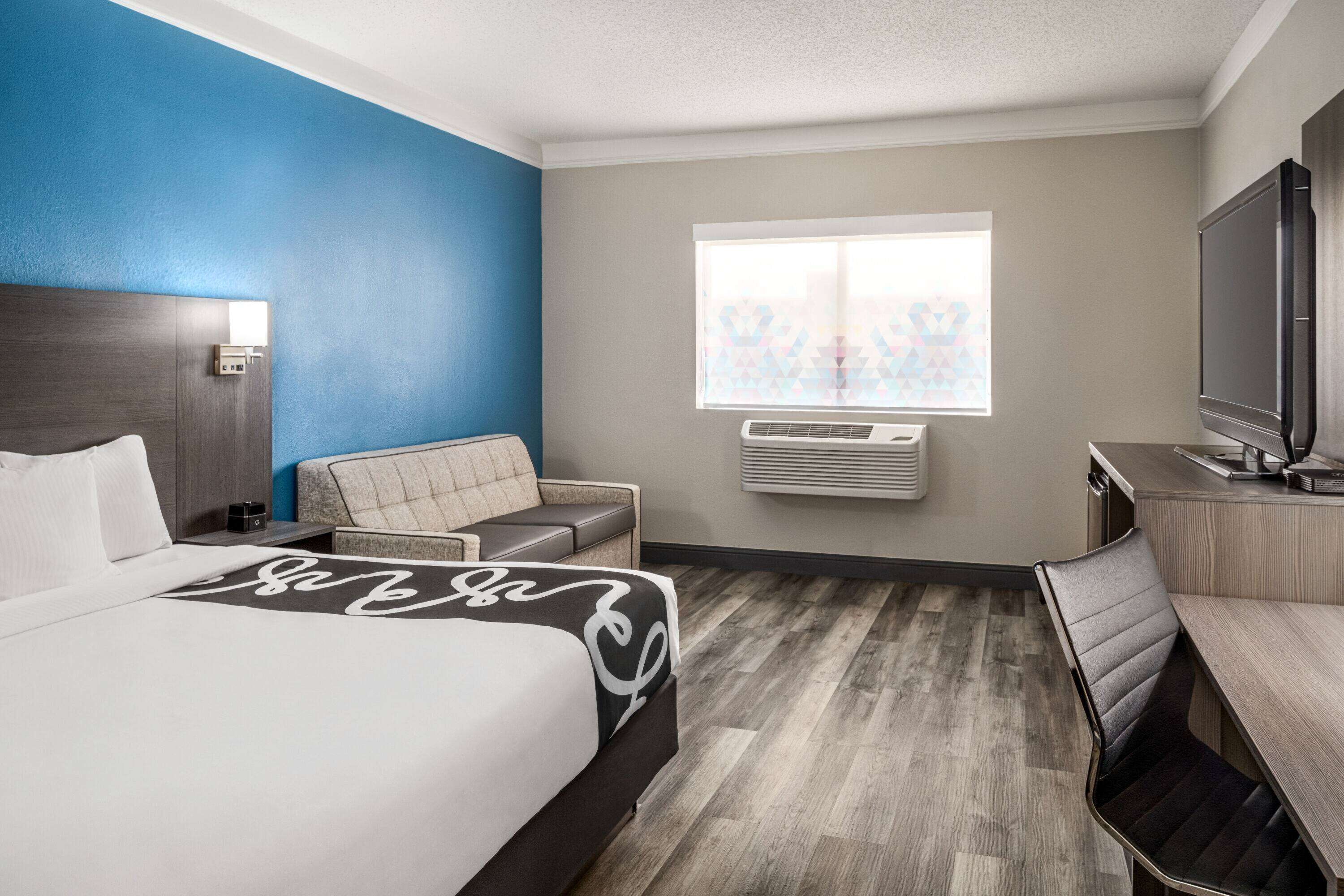 A hotel room with a bed, a desk, a chair, a television, and a window with blinds.