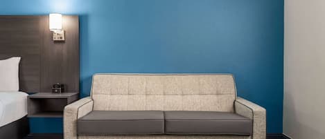A hotel room with a bed, a sofa, a nightstand, and a wall-mounted lamp.