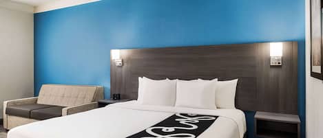 Une chambre d’hôtel avec un grand lit, une table de chevet, un canapé et une lampe fixée au mur.