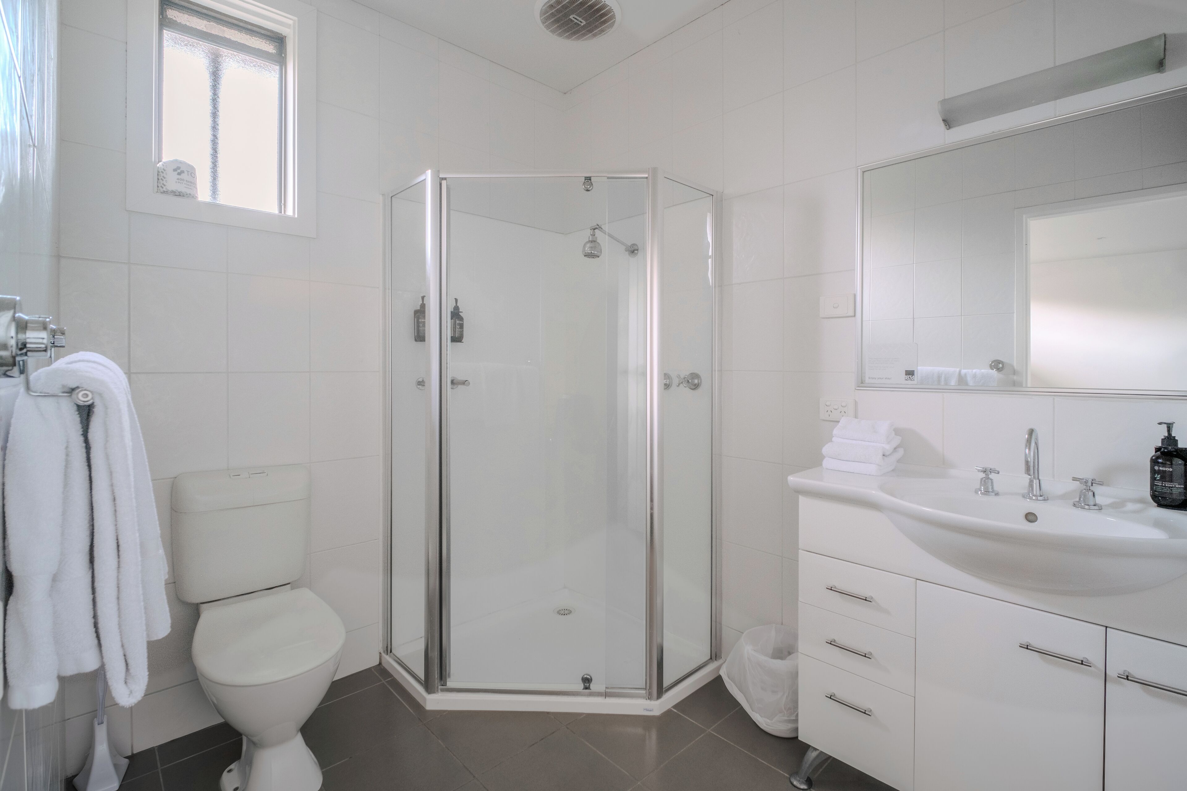 A modern bathroom with a glass-enclosed shower, a white toilet, and a sink with a mirror above it.