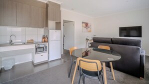 A modern kitchen with white cabinets, a dining table with chairs, and a black sofa in a living area. - Wyndhamere Motel Shepparton (Shepparton)