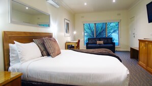 A hotel room with a large bed, a small table, a sofa, and a window with a view of trees. - Wyndhamere Motel Shepparton (Shepparton)