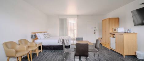 A hotel room with a bed, two chairs, a desk, a television, and a kitchenette.