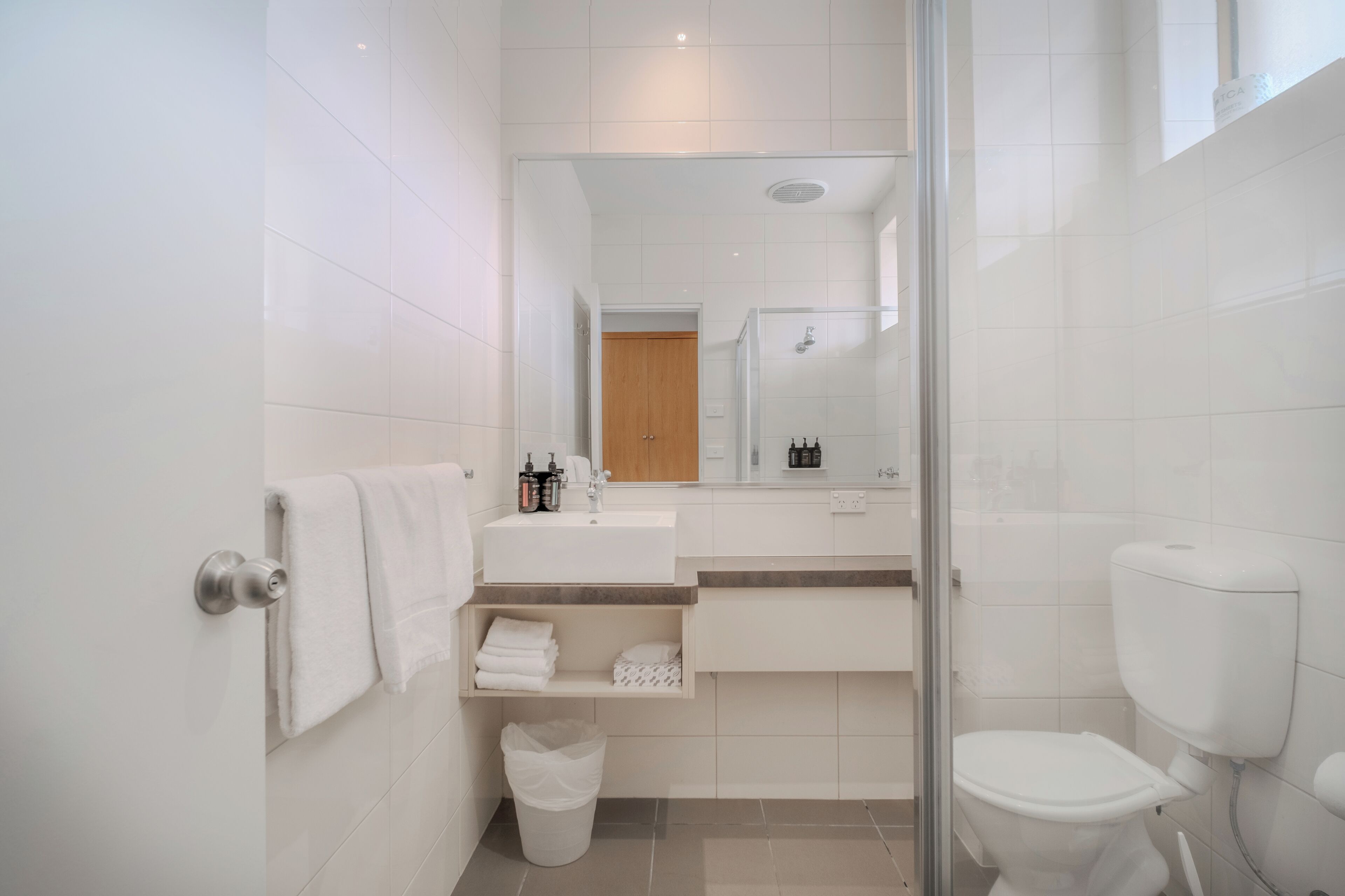A modern bathroom with a glass shower enclosure, a white toilet, and a vanity with a mirror.