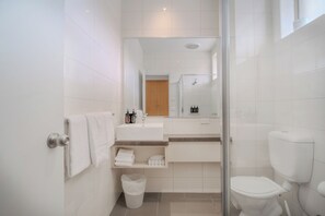 Une salle de bain moderne avec une douche à parois de verre, des toilettes blanches et un meuble-lavabo avec un miroir.