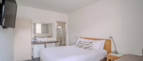 Una habitación de hotel con cama, mesita de noche, escritorio, espejo y televisión.