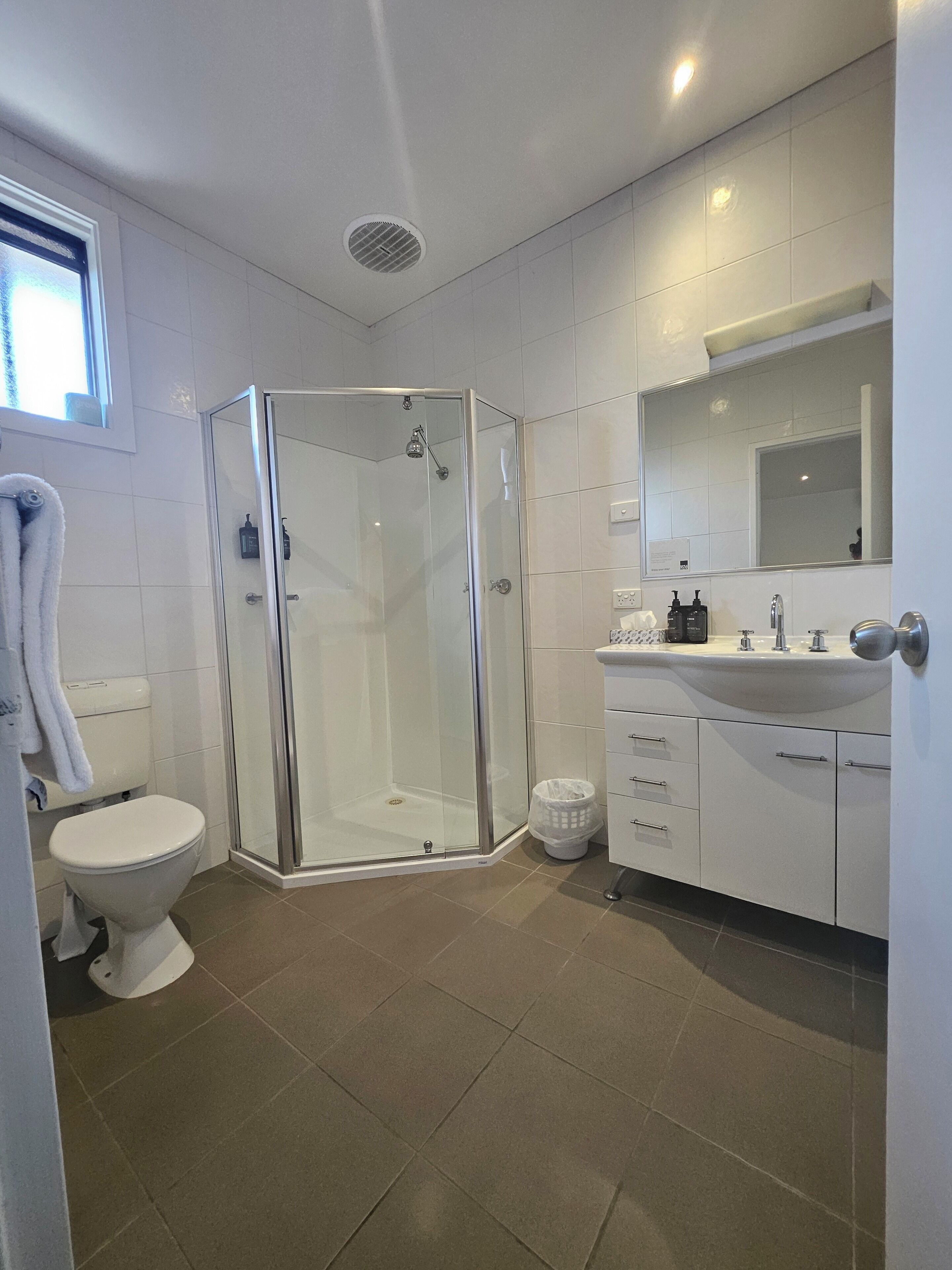 A modern bathroom with a glass-enclosed shower, a toilet, and a sink with a mirror above it.