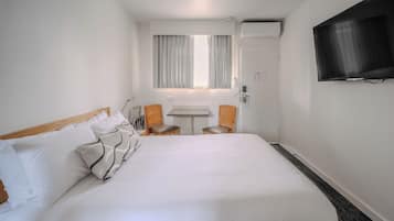 Habitación de hotel con una cama grande, una mesita, dos sillas, un televisor y una ventana con cortinas.