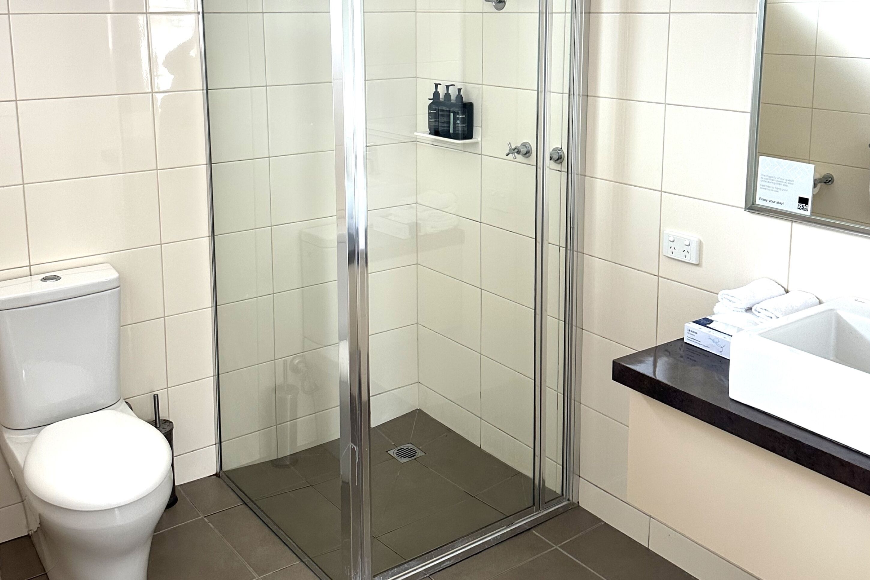 Un baño con ducha de vidrio, inodoro y lavamanos con espejo.