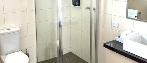 Un baño con ducha de vidrio, inodoro y lavamanos con espejo.