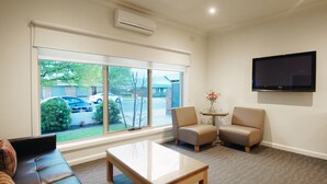 A modern living room with a large window, a flat-screen TV, two armchairs, a sofa, and a coffee table. - Wyndhamere Motel Shepparton (Shepparton)