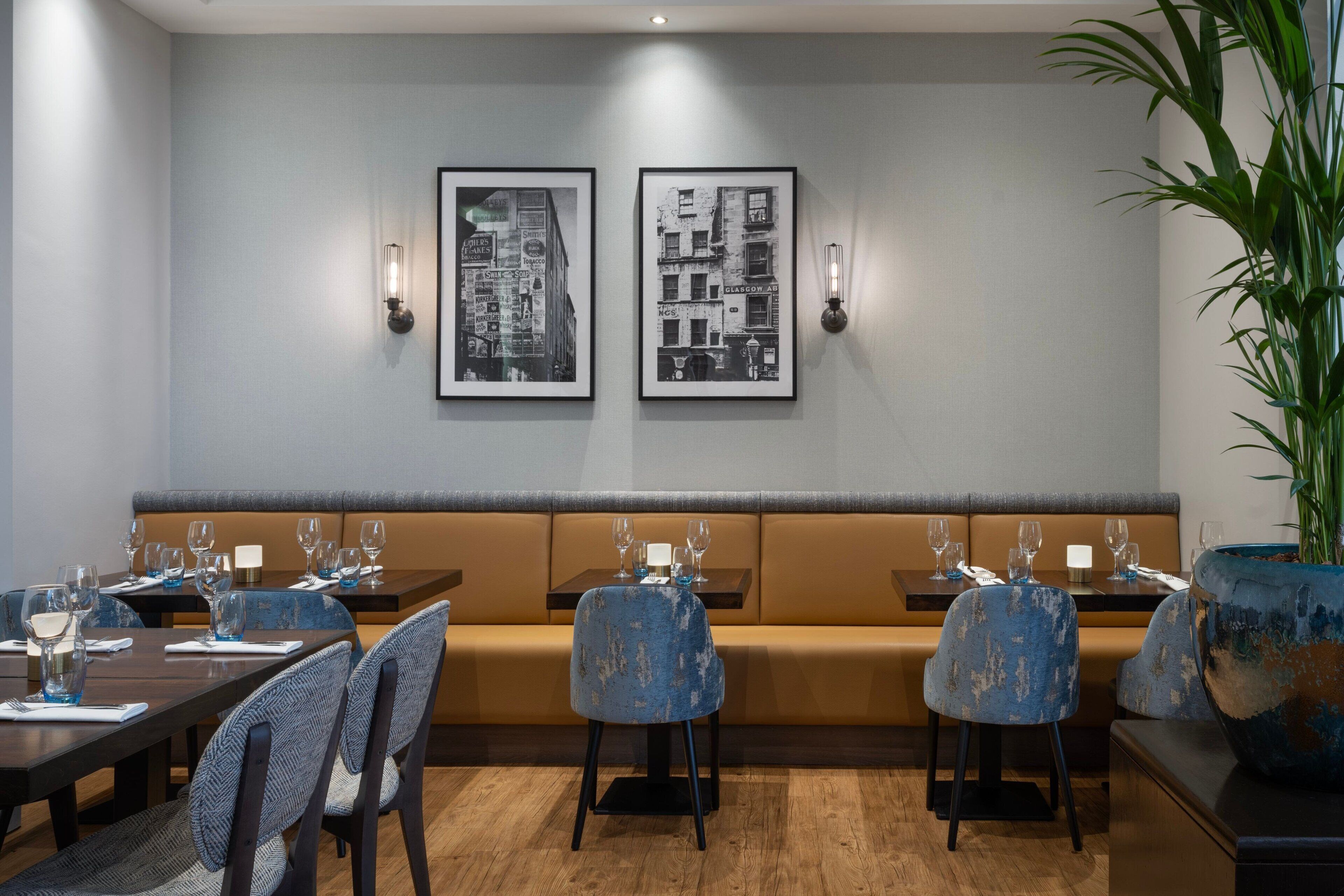 Un restaurante con una barra larga, sillas azules y un sofá. Hay cuadros enmarcados en la pared y una planta en maceta a la derecha.
